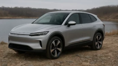 На зображенні зображено електричний SUV, що стоїть на кам'янистій місцевості біля водойми.
