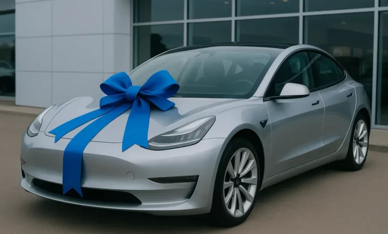 The image features a silver electric vehicle positioned prominently in a car dealership, adorned with a large blue bow on th…