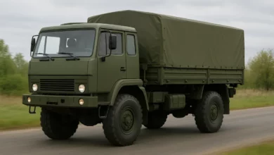 На зображенні зображено військову вантажівку з простим кузовом, яка рухається по дорозі.